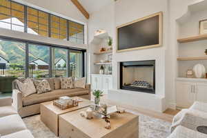 Living room featuring built in features, high vaulted ceiling, a fireplace with raised hearth, beam ceiling, and light wood-style flooring