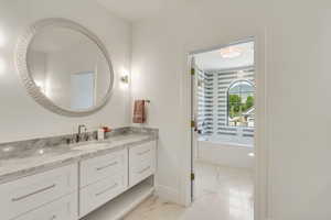 Full bathroom featuring marble look tiles, vanity, and a bath