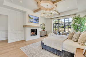 Bedroom featuring a decorative wall, a chandelier, light wood-style flooring, coffered ceiling, and a glass covered fireplace