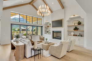 Living room with beam ceiling, high vaulted ceiling, light wood-type flooring, a fireplace, and a chandelier