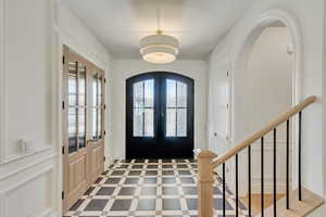 Foyer entrance featuring a decorative wall, french doors, arched walkways, and stairway