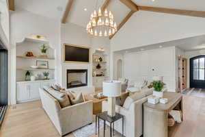 Living room with built in features, high vaulted ceiling, light wood-style floors, beamed ceiling, and a chandelier