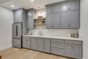 Kitchen featuring freestanding refrigerator, gray cabinetry, decorative backsplash, light wood-style floors, and recessed lighting