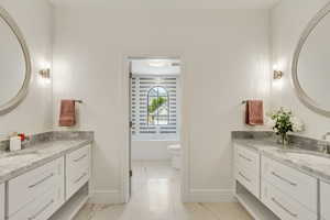 Full bathroom with marble finish flooring, two vanities, and a bath