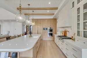 Kitchen with a sink, light wood-style flooring, appliances with stainless steel finishes, light countertops, and wooden ceiling with exposed beams