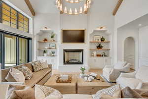 Living room featuring built in shelves, beamed ceiling, a fireplace with raised hearth, a towering ceiling, and a chandelier