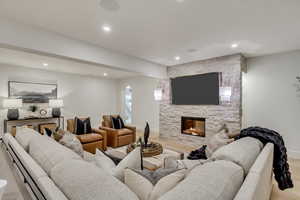 Living area with a stone fireplace, recessed lighting, light wood-style flooring, beam ceiling, and arched walkways