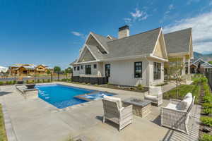 View of pool featuring an outdoor living space with a fire pit, a patio area, a fenced backyard, and a pool with connected hot tub
