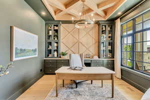 Office space featuring light wood-style flooring, a chandelier, coffered ceiling, and beam ceiling