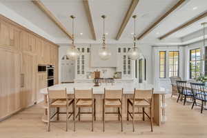 Kitchen featuring beamed ceiling, light brown cabinets, glass insert cabinets, light countertops, and a spacious island