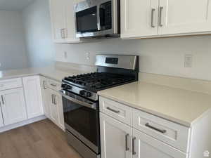 Kitchen with appliances with stainless steel finishes, white cabinetry, wood finished floors, and light countertops