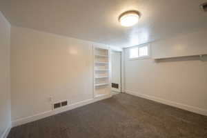 Basement with a textured ceiling, carpet, baseboards, and built in features