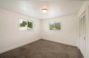 Unfurnished bedroom with multiple windows, baseboards, and dark colored carpet