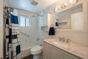 Bathroom featuring vanity, shower / bath combo with shower curtain, toilet, and tasteful backsplash