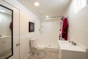 Full bathroom with vanity, a textured ceiling, toilet, a shower stall, and tile patterned flooring