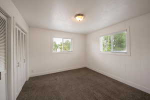 Unfurnished bedroom featuring multiple windows, dark carpet, and baseboards