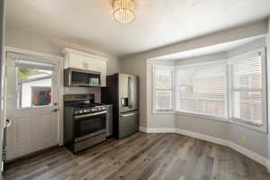 Kitchen featuring appliances with stainless steel finishes, baseboards, white cabinetry, wood finished floors, and a chandelier