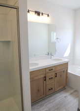Full bath featuring wood finished floors, double vanity, a garden tub, and a shower stall