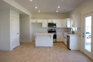 Kitchen featuring stainless steel appliances, a sink, a center island, light wood finished floors, and white cabinetry