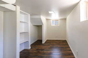 Basement with dark wood-type flooring, baseboards, and built in shelves