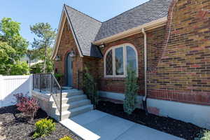 View of exterior entry with roof with shingles and brick siding