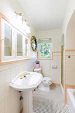 Full bathroom with tile walls, a bathtub, toilet, an enclosed shower, and a wainscoted wall