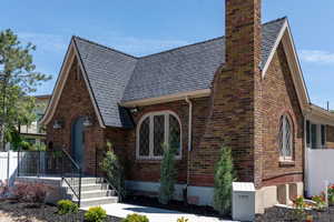 Tudor-style house with a chimney, a shingled roof, and brick siding