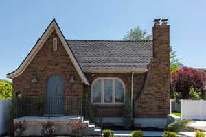 View of front of house featuring brick siding, a chimney, and a shingled roof