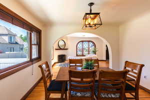 Dining area featuring arched walkways, a chandelier, light wood-style flooring, baseboards, and a fireplace with raised hearth