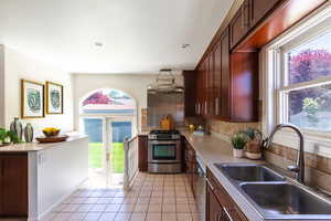 Kitchen featuring a sink, gas stove, tasteful backsplash, light tile patterned flooring, and light countertops