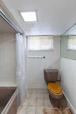 Bathroom featuring toilet, shower / bathtub combination with curtain, and tile patterned floors