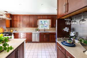 Kitchen with appliances with stainless steel finishes, a sink, decorative backsplash, light tile patterned floors, and decorative light fixtures