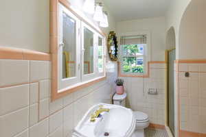 Bathroom featuring tile walls, toilet, a shower stall, a sink, and a wainscoted wall