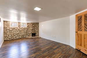 Unfurnished living room with dark wood-style flooring, a stone fireplace, and baseboards