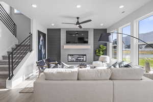 Living area with wood finished floors, recessed lighting, ceiling fan, a large fireplace, and stairway