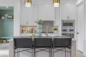 Kitchen with stainless steel appliances, white cabinetry, light countertops, decorative backsplash, and decorative light fixtures