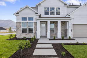 Craftsman house with stone siding, covered porch, a front lawn, a mountain view, and concrete driveway