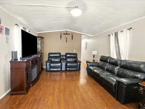 Living room featuring wood finished floors, vaulted ceiling, baseboards, and a textured ceiling