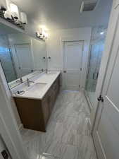 Bathroom featuring marble finish floors, double vanity, and a stall shower