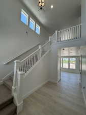 Stairs with plenty of natural light, a towering ceiling, wood finished floors, a chandelier, and baseboards