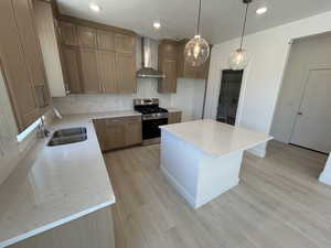 Kitchen featuring gas range, wall chimney exhaust hood, a sink, tasteful backsplash, and a kitchen island