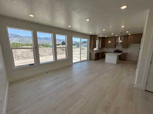 Kitchen featuring wall chimney exhaust hood, a center island, open floor plan, light wood-style flooring, and recessed lighting
