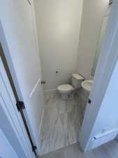 Half bath featuring marble look tile flooring, toilet, and baseboards