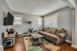 Living room featuring arched walkways, hardwood / wood-style flooring, a textured ceiling, and baseboards
