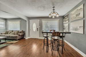 Dining room with dark wood-style floors, a textured ceiling, baseboards, arched walkways, and a chandelier