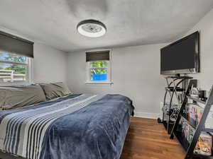 Bedroom with multiple windows, wood finished floors, a textured ceiling, and baseboards