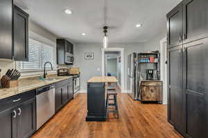 Kitchen with stainless steel appliances, a sink, recessed lighting, light stone counters, and dark wood finished floors