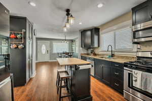 Kitchen featuring stainless steel appliances, a sink, recessed lighting, a kitchen bar, and dark wood-type flooring