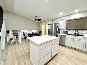 Kitchen with appliances with stainless steel finishes, a sink, ceiling fan, light wood finished floors, and white cabinetry