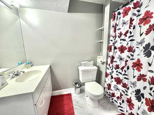 Full bath featuring vanity, toilet, marble look tiles, baseboards, and a shower with shower curtain